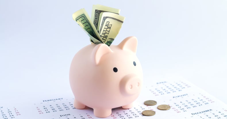 Putting a one hundred dollar bill into a piggy bank to jumpstart longterm savings goals.