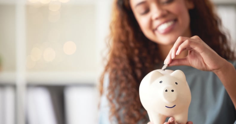 An image of a smiling woman putting a coin in a piggy bank.