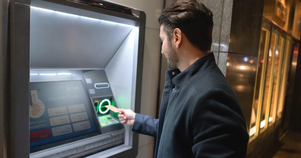 A man standing at an ATM putting his debit card into the green card slot